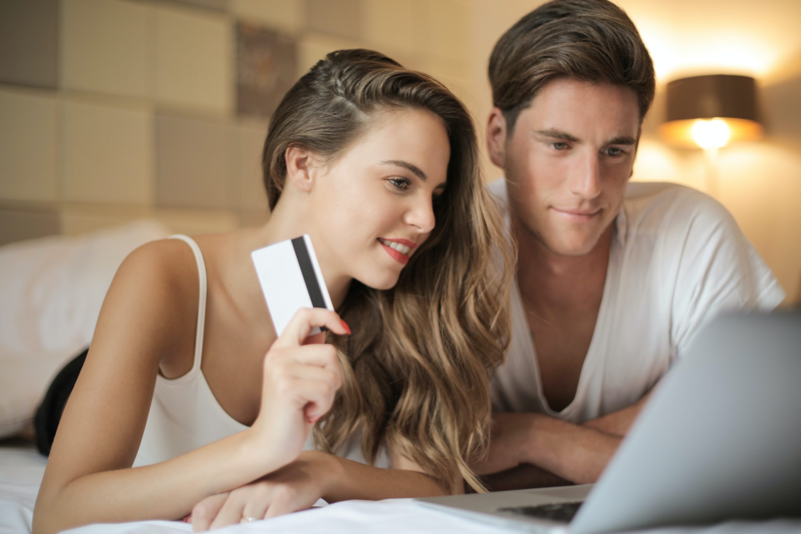 Ein junges Paar sitzt auf einem Bett vor einem Laptop. Die Kreditkarte in der Hand der Dame zeigt, dass sie zusammen einen Online-Kauf tätigen wollen. Das Bild soll verdeutlichen, dass Customer Centricity einen direkten Einfluss auf die Zufriedenheit der Kund:innen hat.